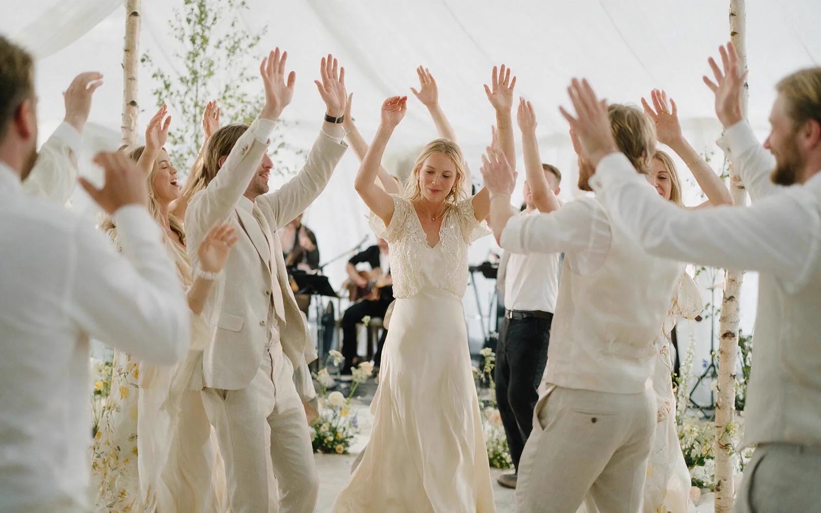 Bryllupsgjester danser med hendene i været i et festtelt, med bandet i bakgrunnen.